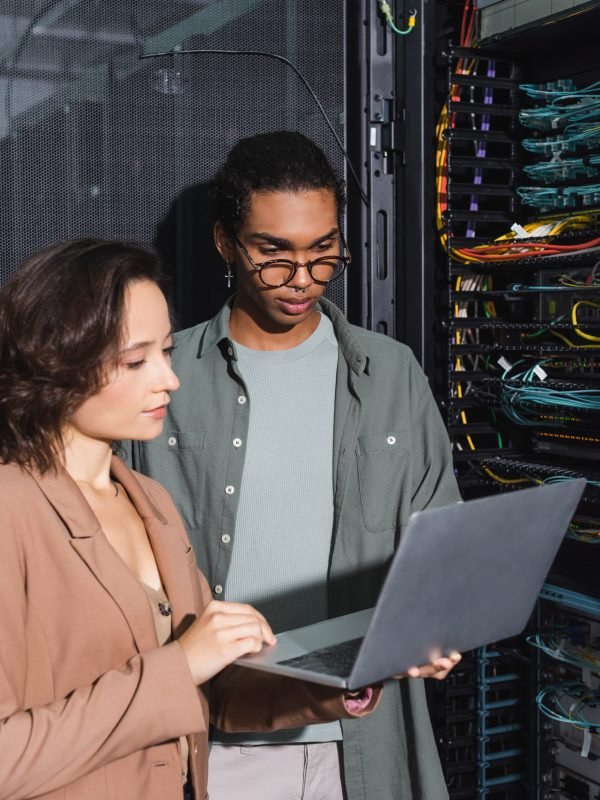 multiethnic technicians working on laptop near server in data center