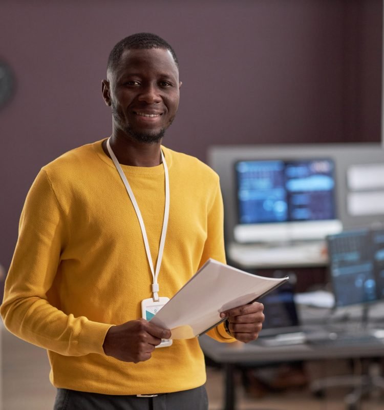 Waist up portrait of smiling black man as IT engineer standing in office, copy space